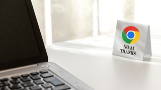 A laptop on a white desk faces a small sign with the Google Chrome logo, saying "No AI Thanks."