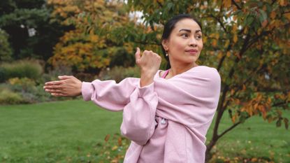 Woman stretching arm across her body standing outside about to do jumping workout