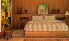 Bed on wood platform against wall with wood panelling and built-in bedside table niches