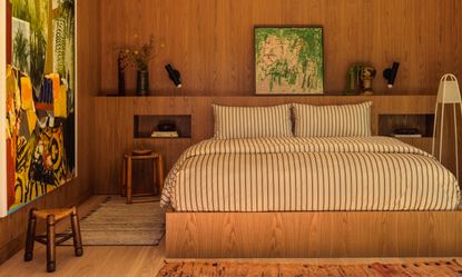 Bed on wood platform against wall with wood panelling and built-in bedside table niches
