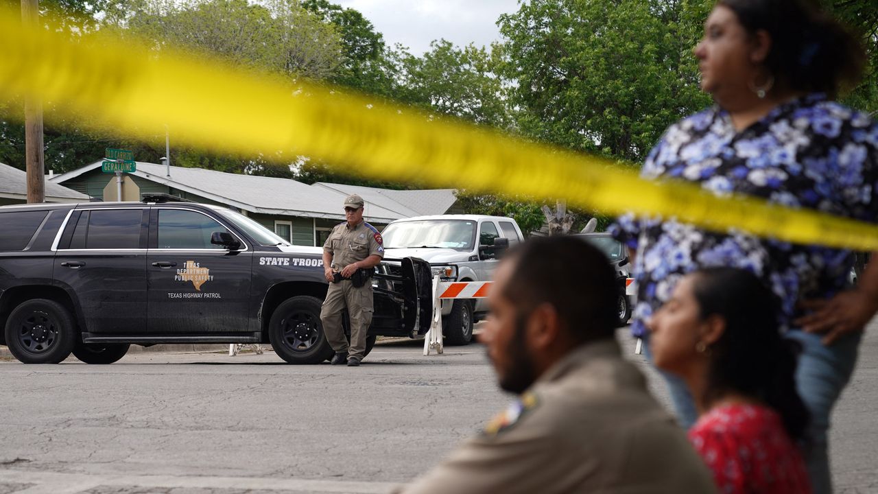 A family sits outside Robb Elementary School with a police officer looking on