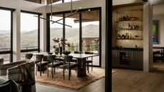 A modern dining space with a home bar and sweeping mountain views through large blame-framed floor to ceiling windows