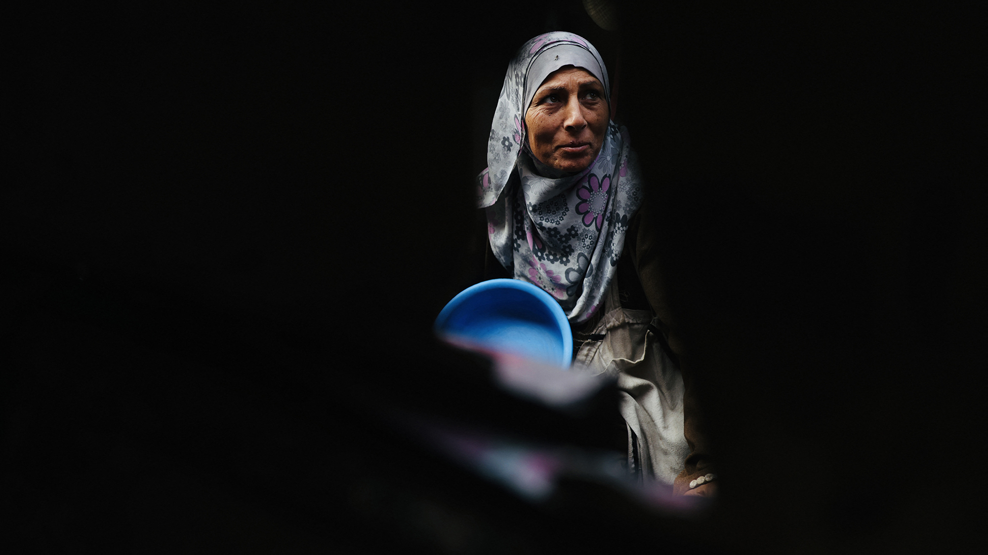 A displaced Palestinian woman waits with her container to receive food at a charity kitchen in Khan Yunis, Gaza Strip