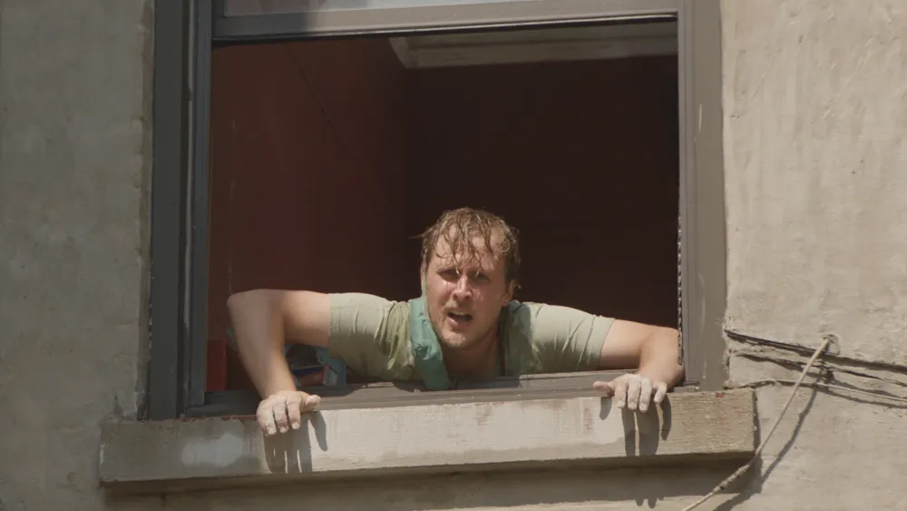 A still from the film Stress Positions of a character leaning out of a window and screaming.