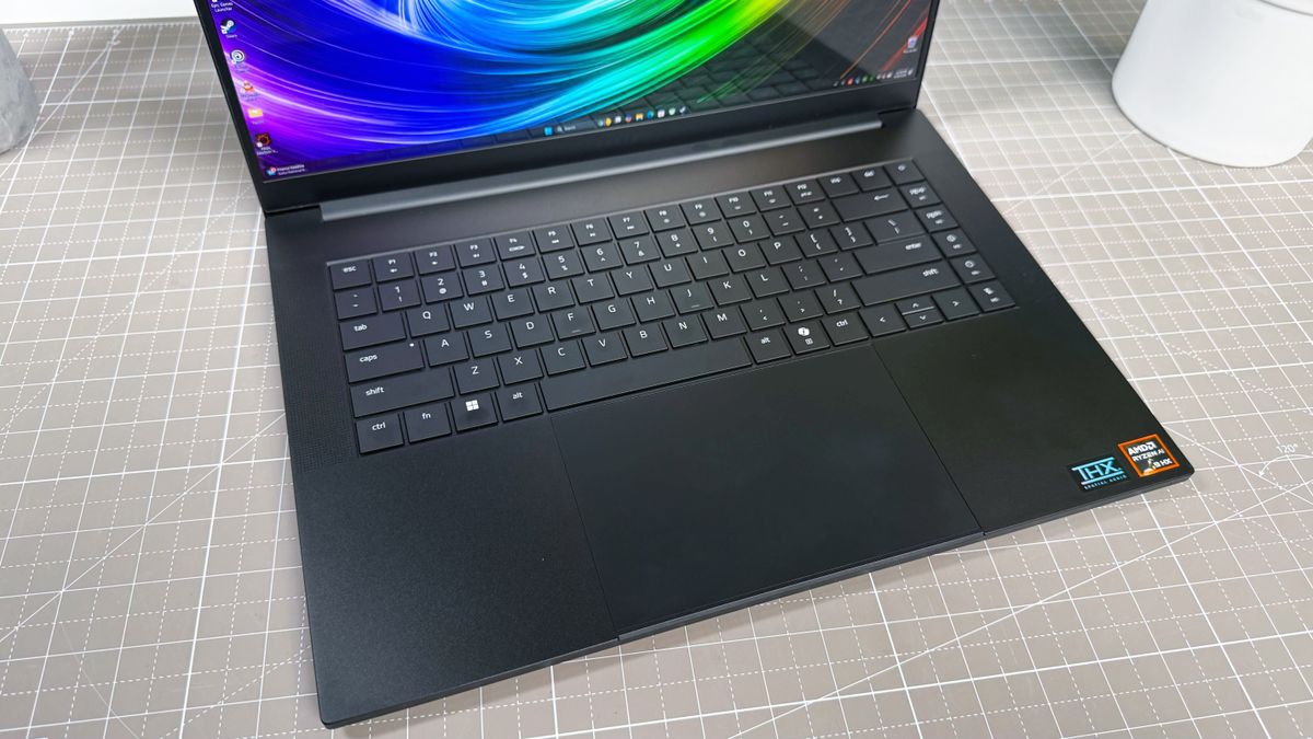 Angled shot of the keyboard deck of the Razer Blade 16 (2025) gaming laptop, on a white and beige desk against a gray backdrop.