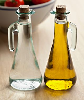 Two tall glass bottles with corks containing white vinegar and oil
