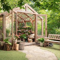 wooden frame greenhouse showing plants and hanging lights with bench outside
