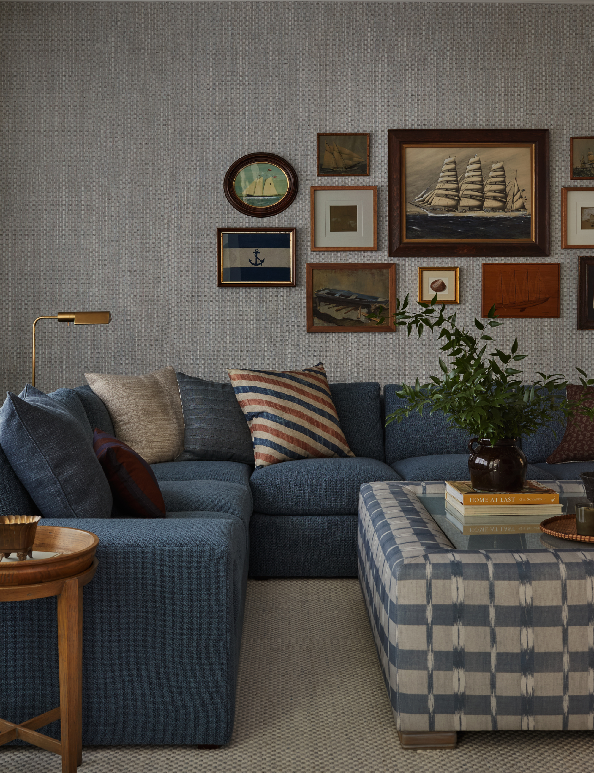 nautically themed living room with a blue sectional sofa, patterned coffee table/ottoman, and antique-style maritime artwork on the walls