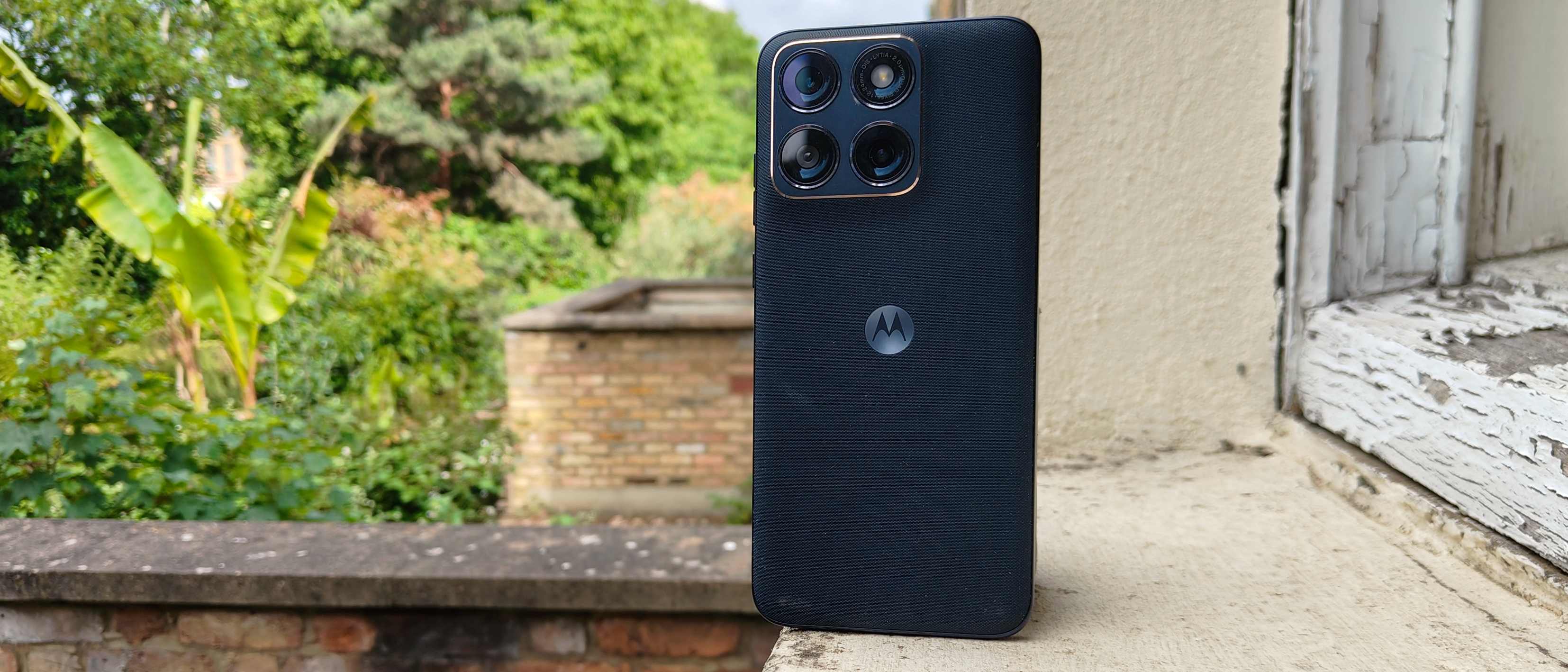 The Motorola Edge 70 Fusion on a window sill, before some bushes.