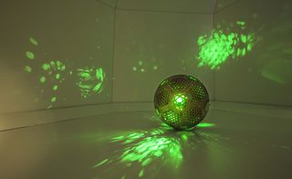 A hollow, wooden ball with mesh-like panels, allowing a green light to shine out