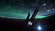 A stunning green aurora wraps around the twinkling Earth at night, with a piece of the International Space Station in the foreground