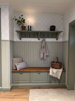 Storage seating in a panelled alcove painted sage green with decorated shelves above