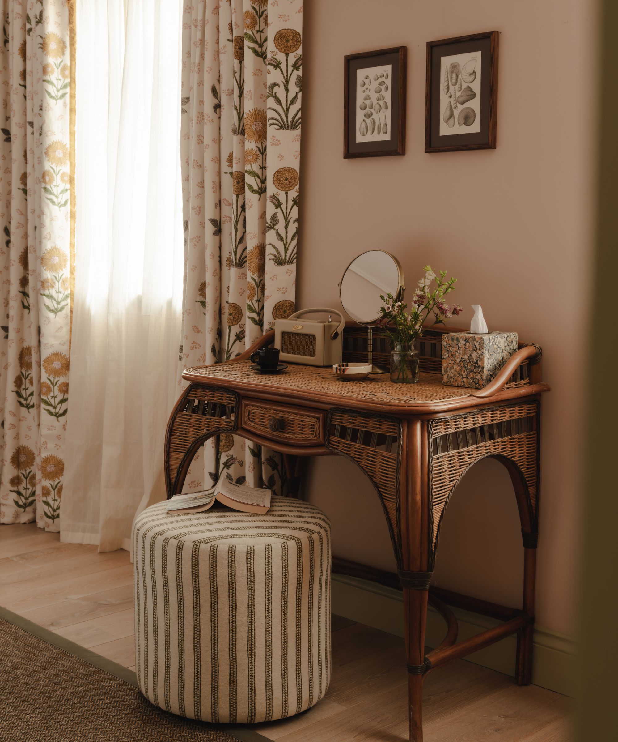 a pale pink and green bedroom with floral curtains and an antique wicker vanity table with striped stool