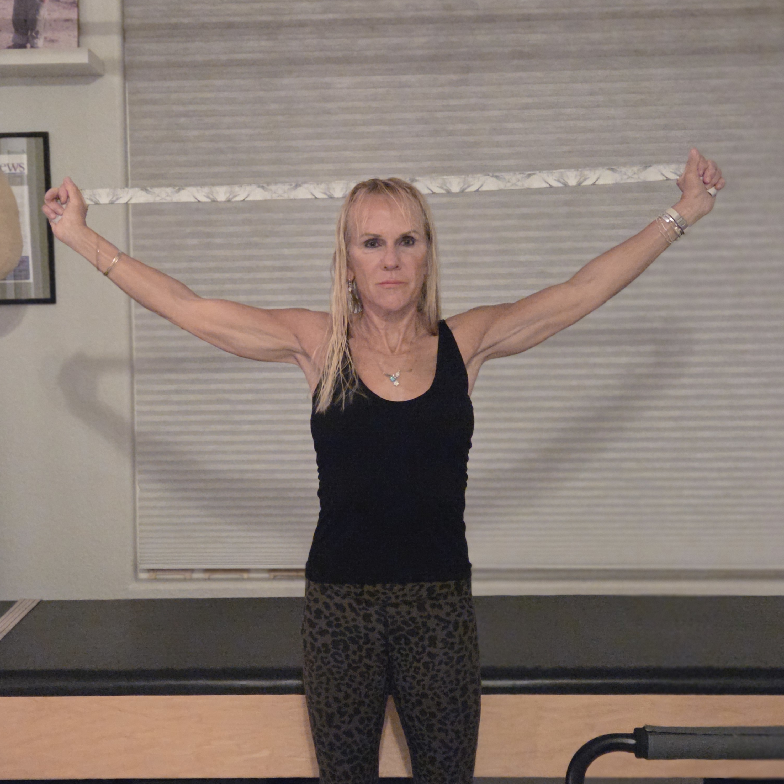 Woman stretching with yoga strap in front of a Pilates reformer bed