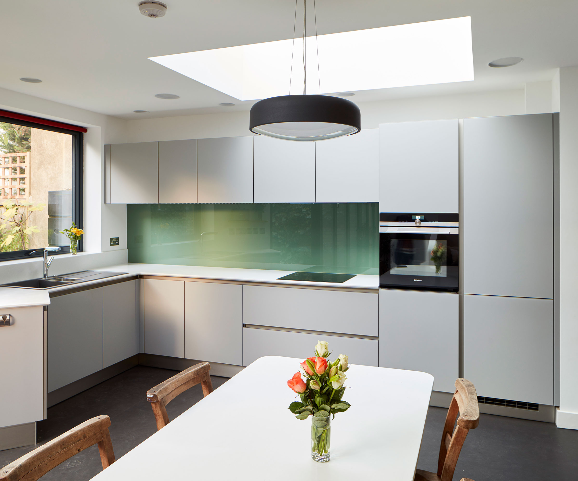 modern white kitchen with green glass splashback and square roof lantern