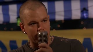 A pierced and shaved Matt Damon speaks into an old school mic on stage in Euro Trip.