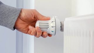Person turning down the thermostat on a radiator