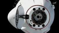 A close-up near the open nosecone of the SpaceX CRS-35 Cargo Dragon spacecraft hangs in the black of space.