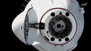 A close-up near the open nosecone of the SpaceX CRS-35 Cargo Dragon spacecraft hangs in the black of space.