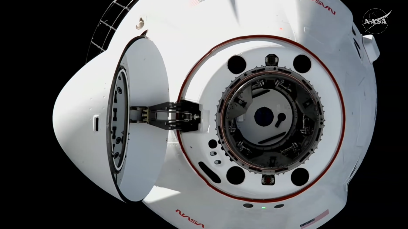 A close-up near the open nosecone of the SpaceX CRS-35 Cargo Dragon spacecraft hangs in the black of space.