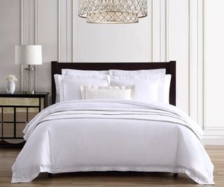 Pure Parima bedding on a bed beneath a chandelier.