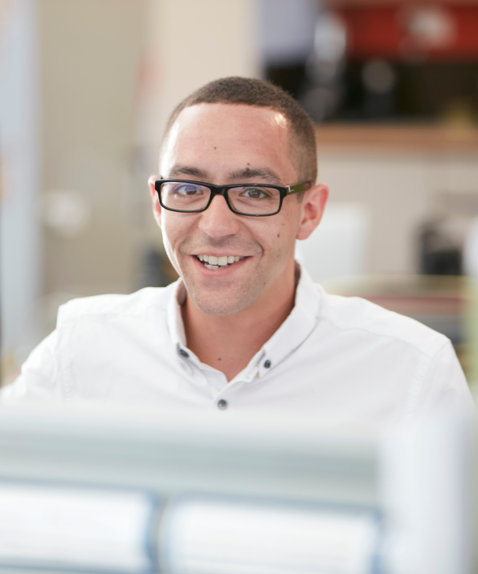 headshot of man in white shirt wearing glasses sat at computer