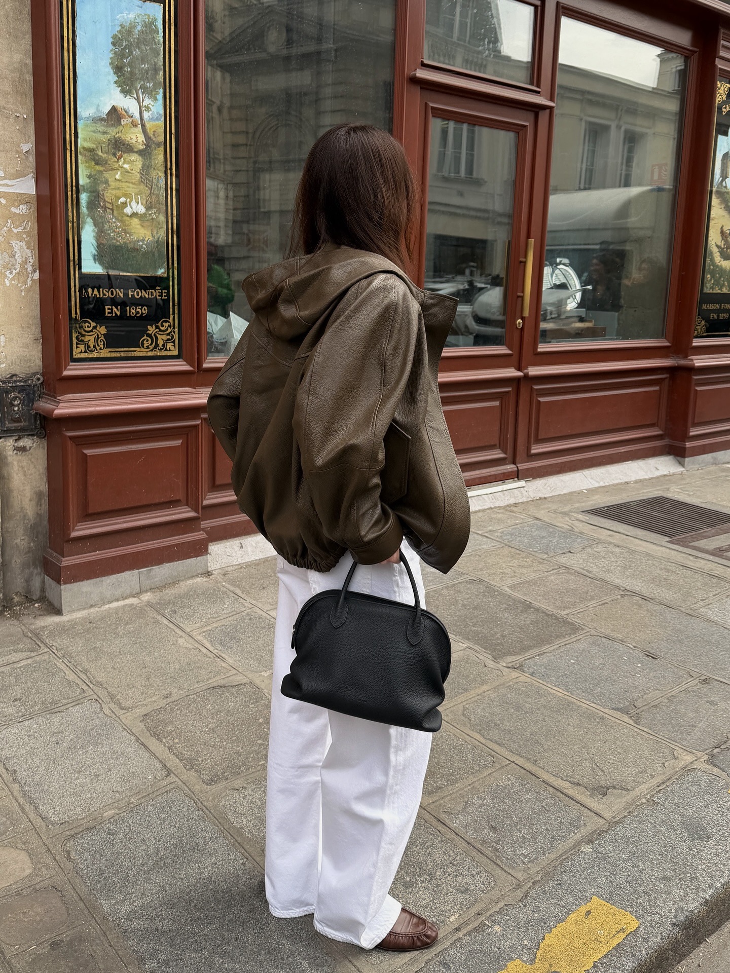 Woman wears leather jacket, white jeans, black bag and loafers