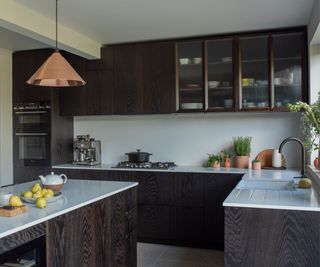 Dark oak kitchen cabinets paired with reeded glass fronted upper cabinets and copper pendant lights