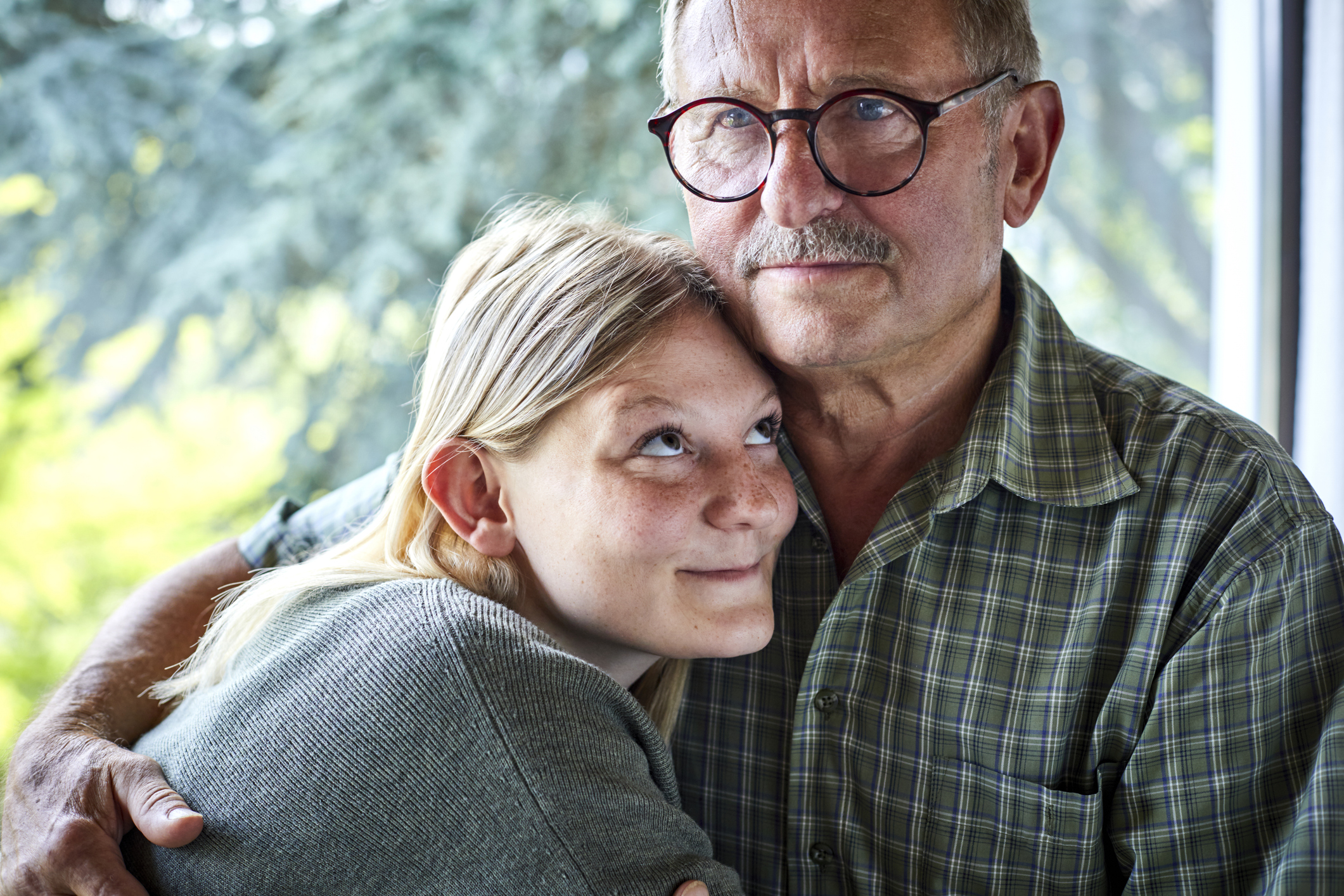 Grandfather hugging adult granddaughter at the window.