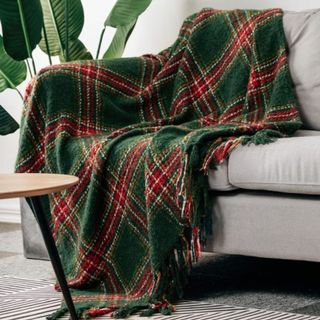Green and red plaid throw blanket on neutral grey sofa and green plant in background