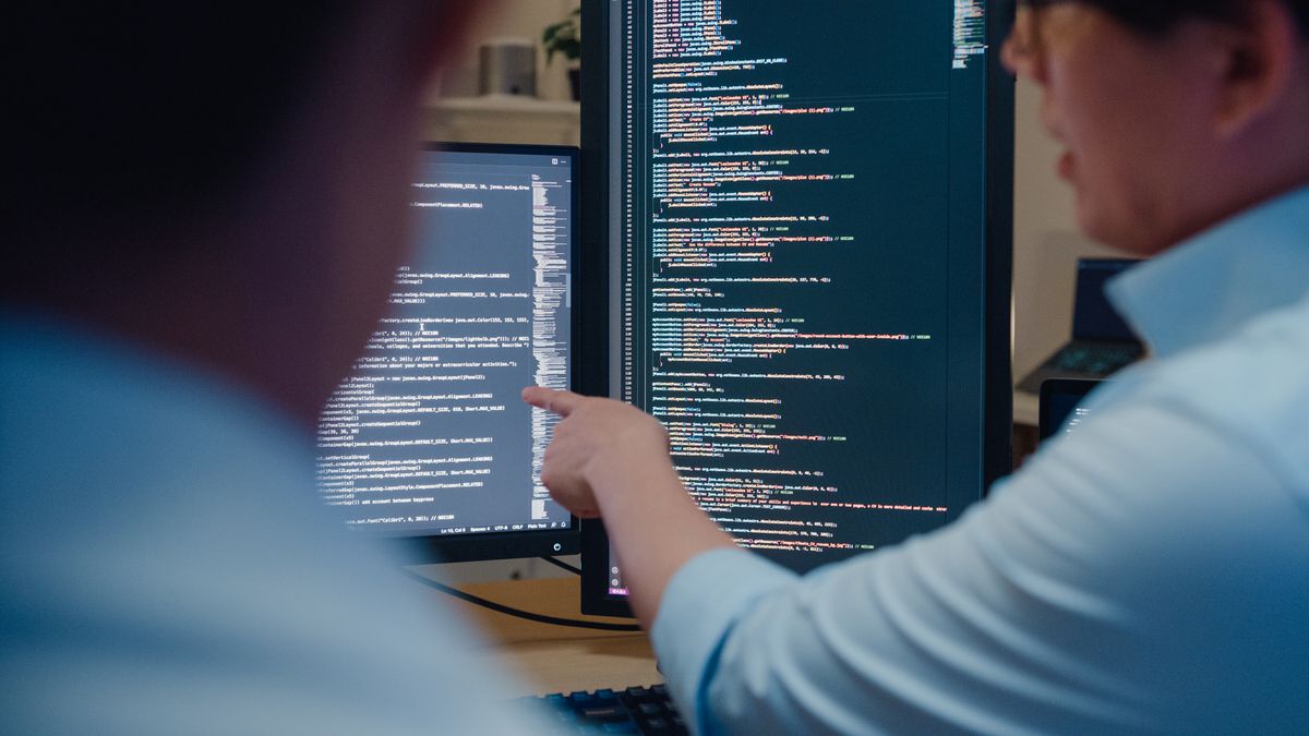 A close up of two software engineers looking at two monitors showing computer code