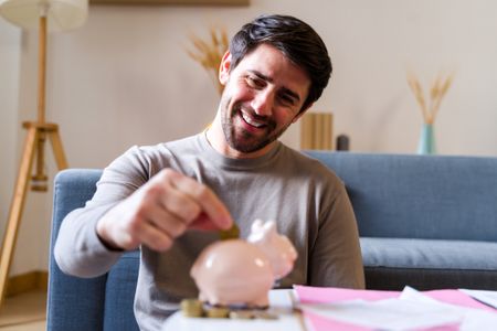 a smiling man depositing coins into a piggy bank