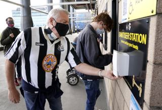 Face mask-wearing Newcastle fans use a hand sanitising station ahead of the Premier League match against Sheffield United at St James’ Park. Despite the season ending on the high of having supporters back in stadia, the experience of attending matches is noticeably different to pre-pandemic conditions. Football fans will have to adapt to a 'new normal' at grounds, with the wait for the return of capacity crowds set to continue for the foreseeable future (Owen Humphreys/PA)