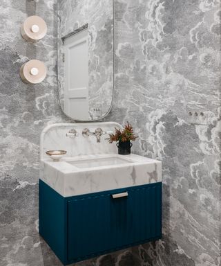 Small bathroom with cloud wallpaper, small vanity with blue cabinetery, wall lights, mirror,