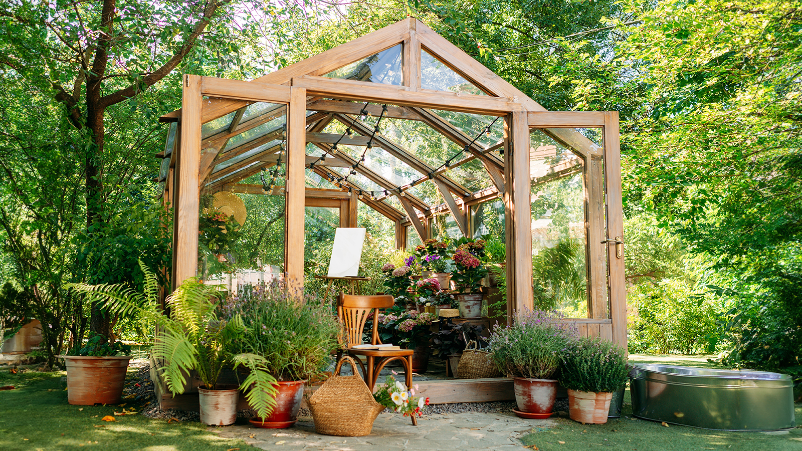 Wooden greenhouse in garden with seat and potted plants