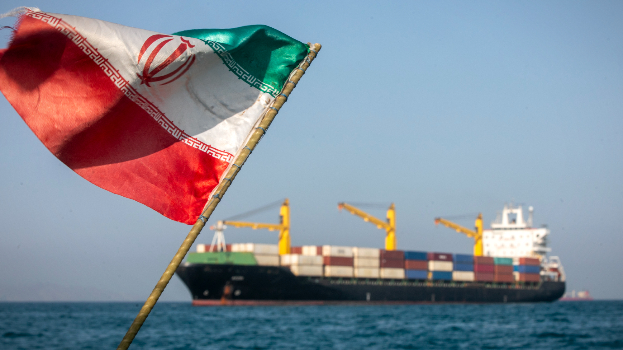 Iranian flag flutters in front of cargo ship transiting the Strait of Hormuz