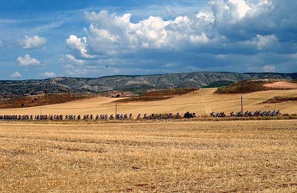 The peloton passes across dry Spanish countryside under partly-cloudy skies