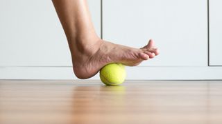 a photo of a foot rolling on a tennis ball - one of the best exercises for plantar fasciitis 