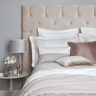 A bed with a large quilted velvet headboard in a bedroom