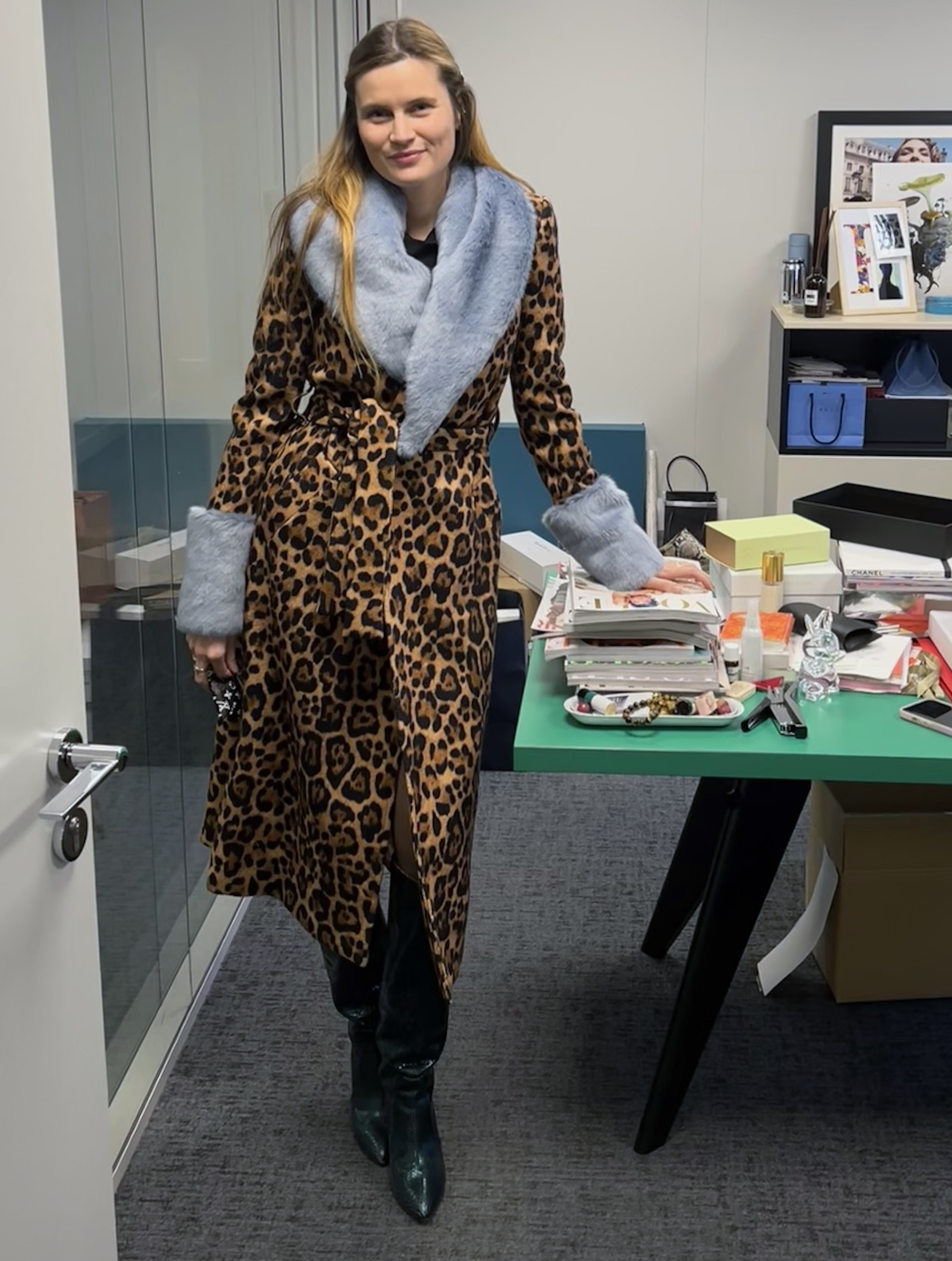 French editor and writer Eugenie Trochu poses in the Vogue France offices wearing a belted leopard-print coat with a blue fur collar and cuffs and patent knee-high boots