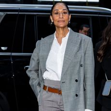 Tracee Ellis Ross wearing a white button up under a grey blazer. She is wearing a slicked back bun and silver hoop earrings.