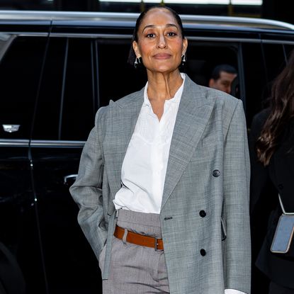 Tracee Ellis Ross wearing a white button up under a grey blazer. She is wearing a slicked back bun and silver hoop earrings.