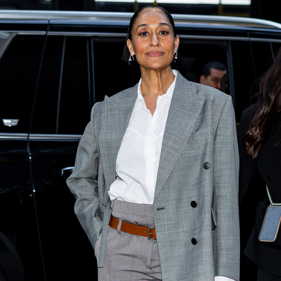 Tracee Ellis Ross wearing a white button up under a grey blazer. She is wearing a slicked back bun and silver hoop earrings.