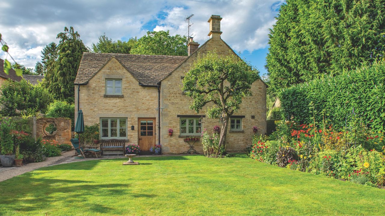 Large grass lawn in garden in front of house. Flowering plants growing in garden border.