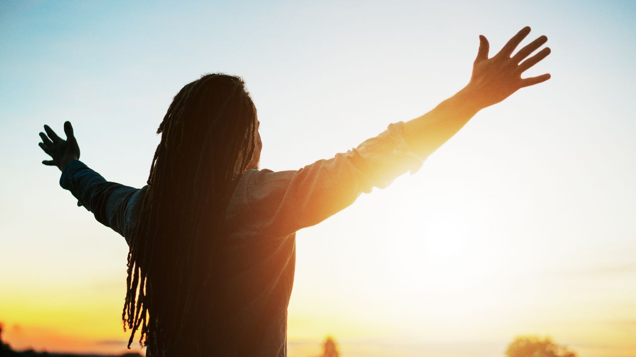 A man faces the sun with his arms open wide.