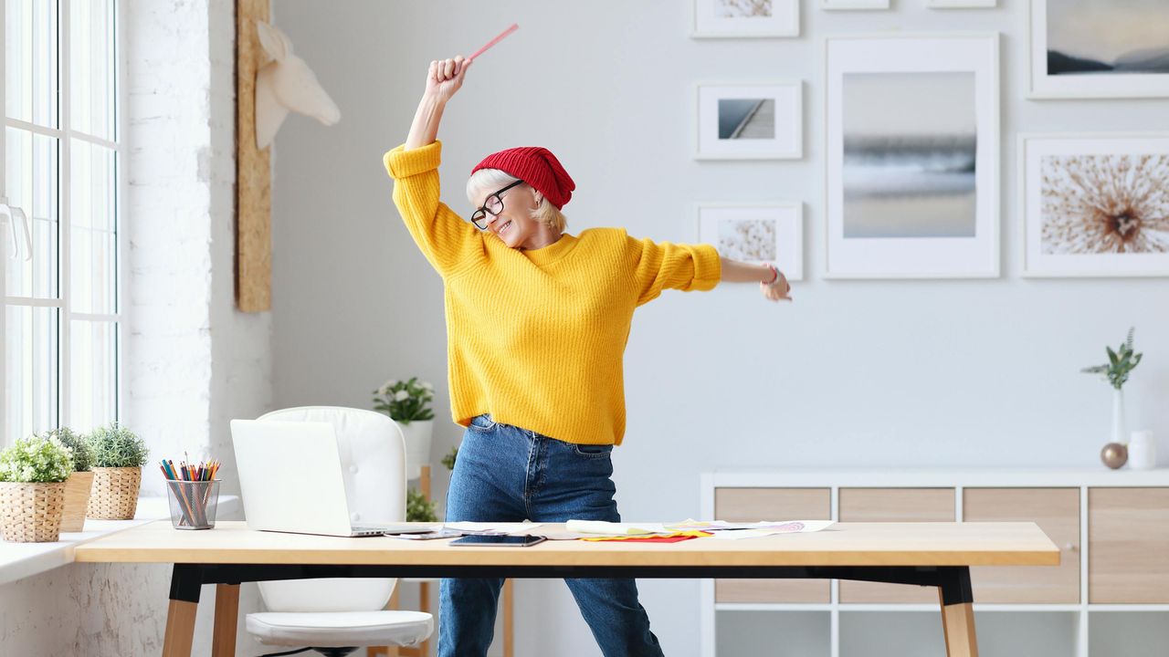 A woman with white hair celebrates joyfully in her shop.