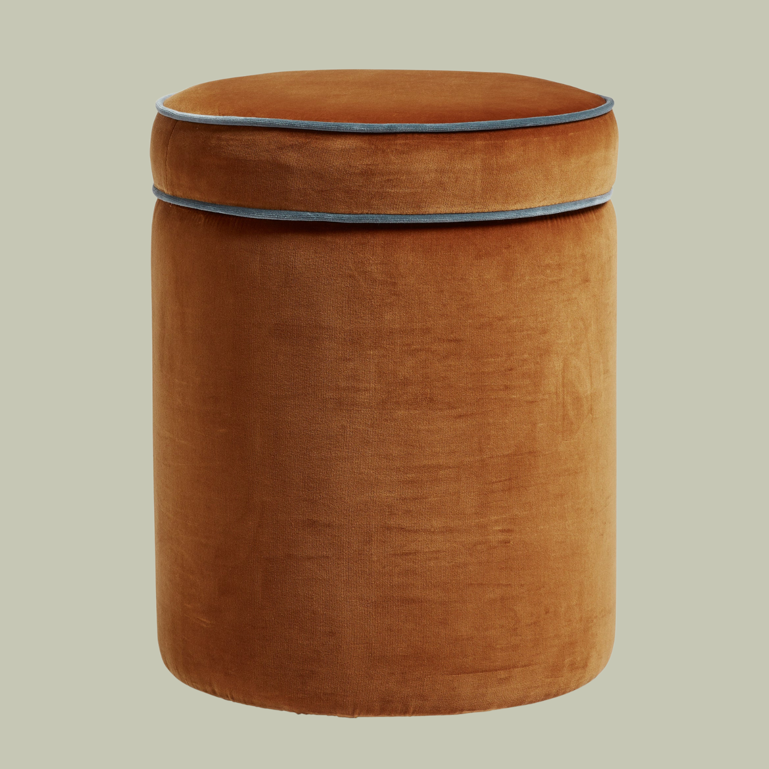 A cinnamon ottoman with a blue lining against a light dusty green background