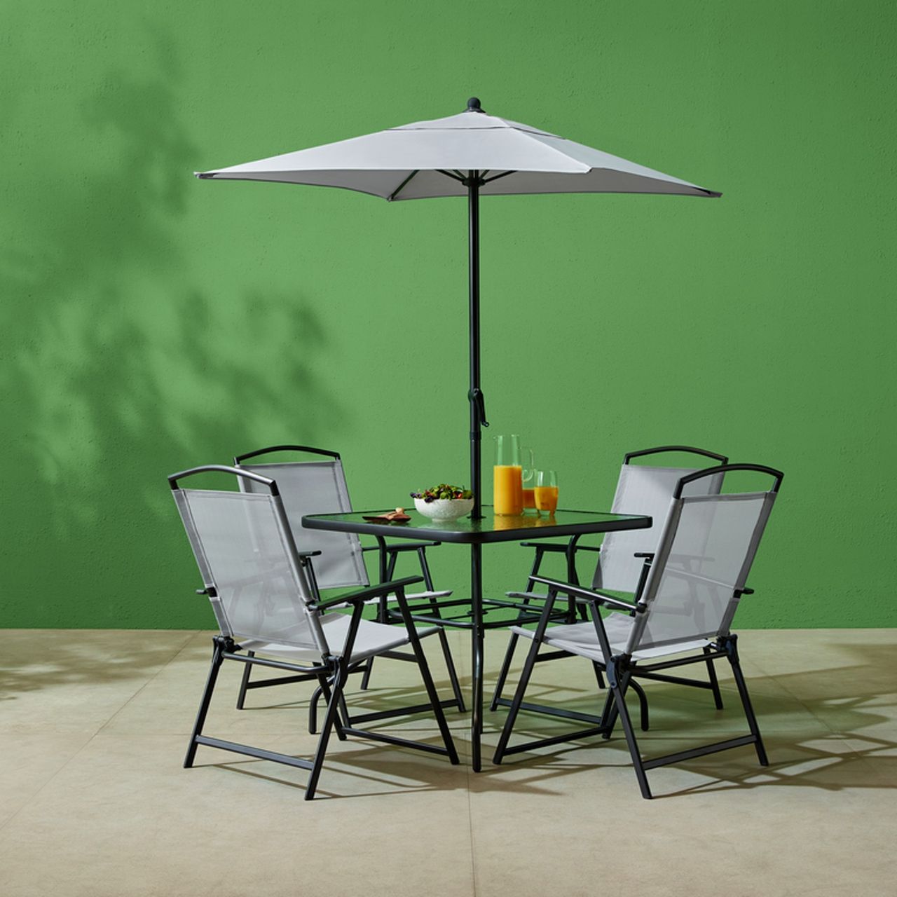 Tesco Outdoor Living 6-piece dining set with food and drinks on table, against a green wall
