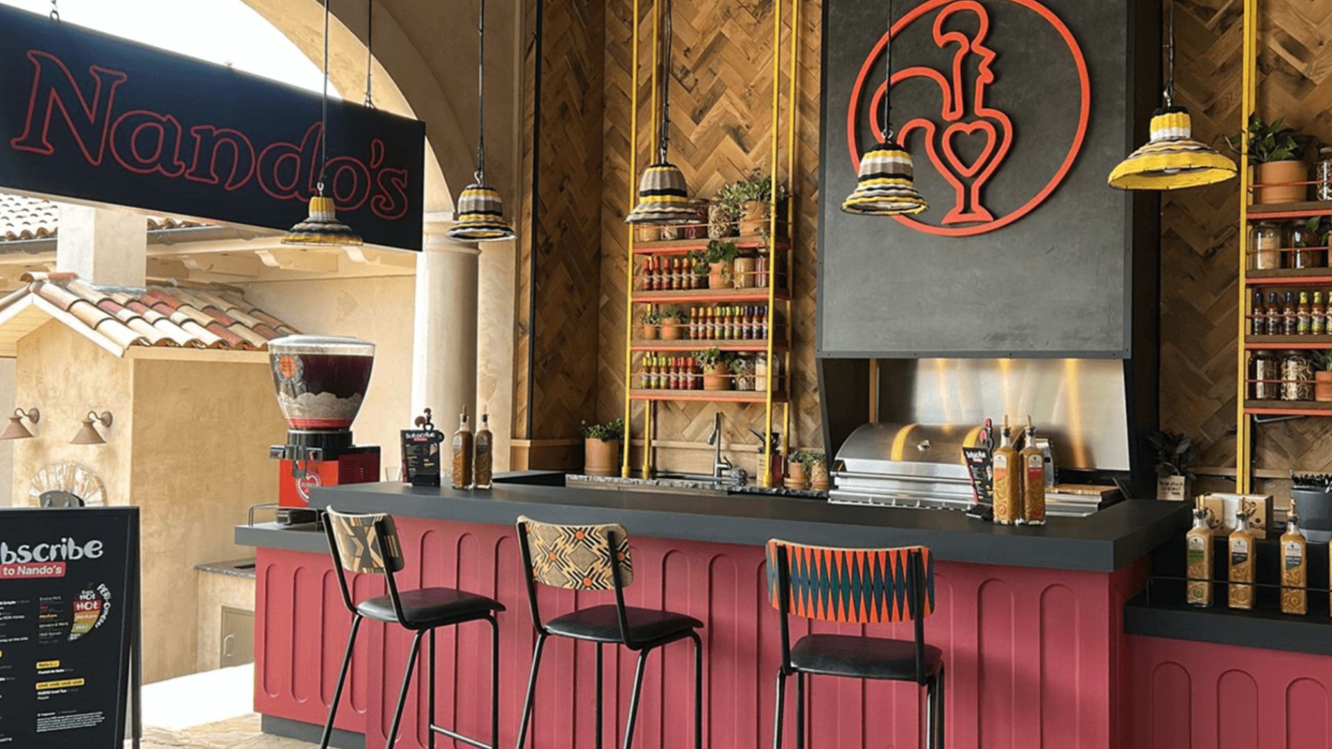 an image of the pop up Nando's restaurant inside the Texas mansion. The logo is hanging on the wall with a sign to the left. There is a bar with three chairs up against it