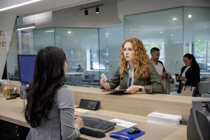 Young female client with debit card talking with bank teller in bank